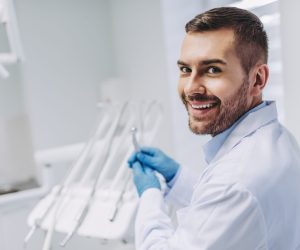 portrait of smiling caucasian dentist holding dental drill and looking at the camera in dental clinic